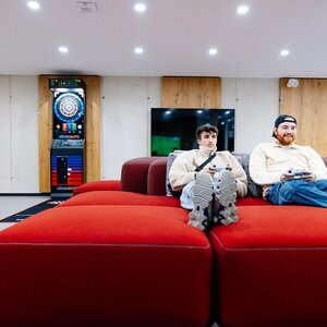 Abbildung zweier Bewohner, die auf einem roten Sitzmöbel sitzen und Videospiele spielen