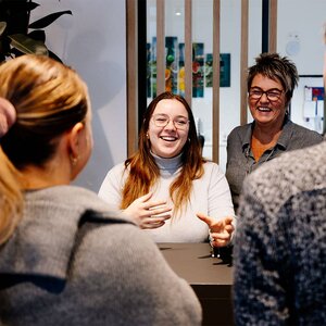 Abbildung zweier MitarbeiterInnen am Empfang, die zwei Gäste empfangen